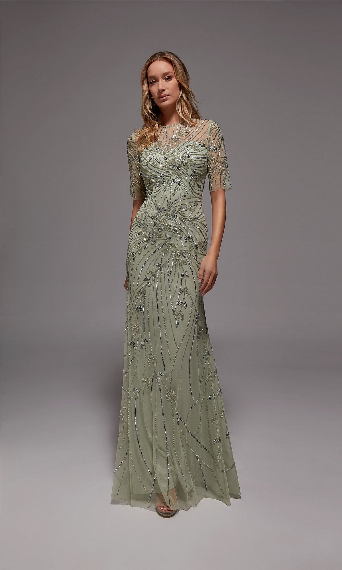 A woman stands against a plain gray background in the Alyce 27809 long formal dress, mint/silver with beaded accents and sheer short sleeves—ideal for formal events or as an elegant mother-of-the-bride gown.